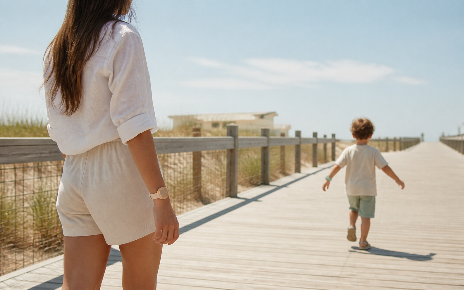 A parent watching a child walk ahead on a beach boardwalk, both wearing Yoonear wristbands.